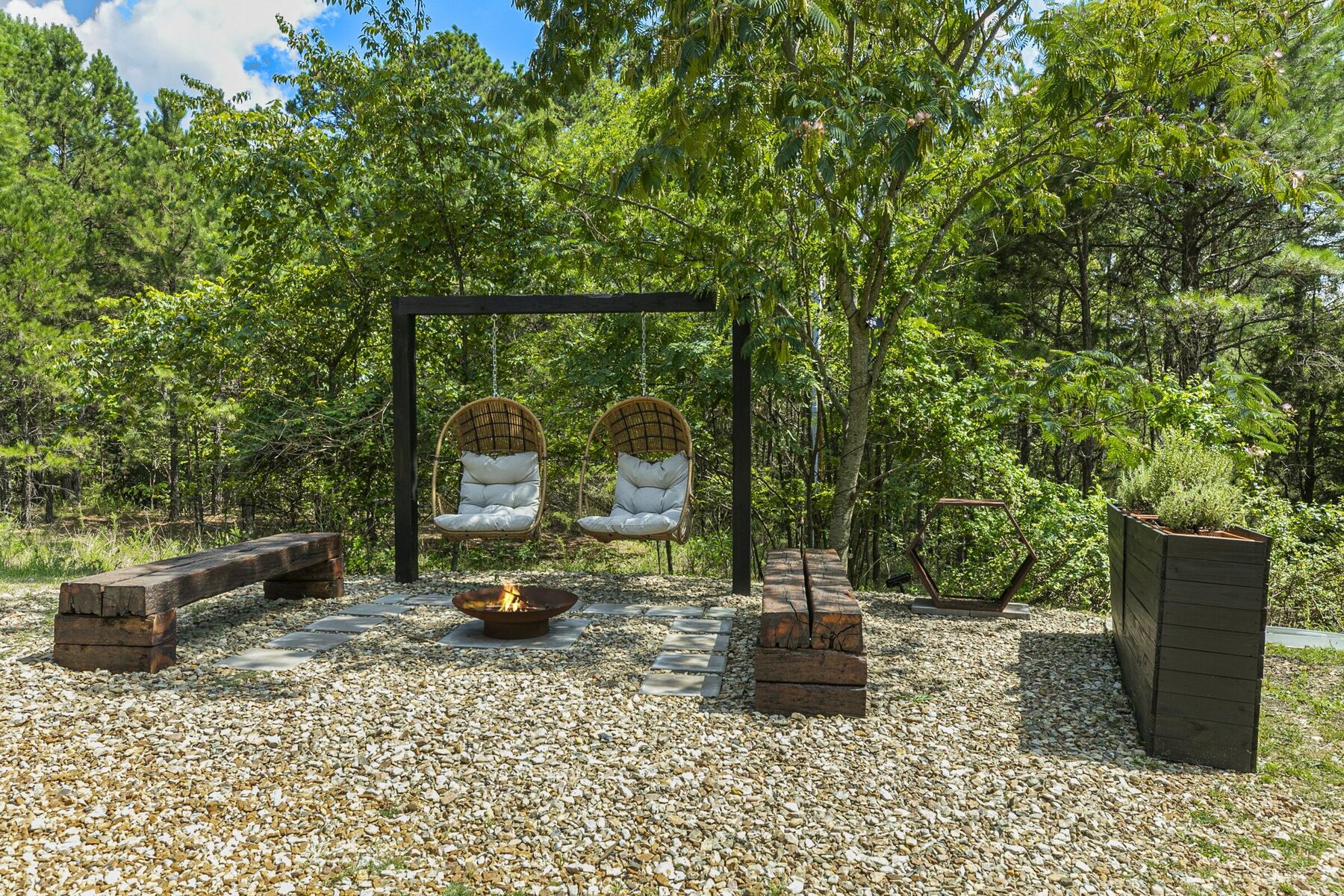 Hanging egg chairs around a fire pit in a wooded corner of the property