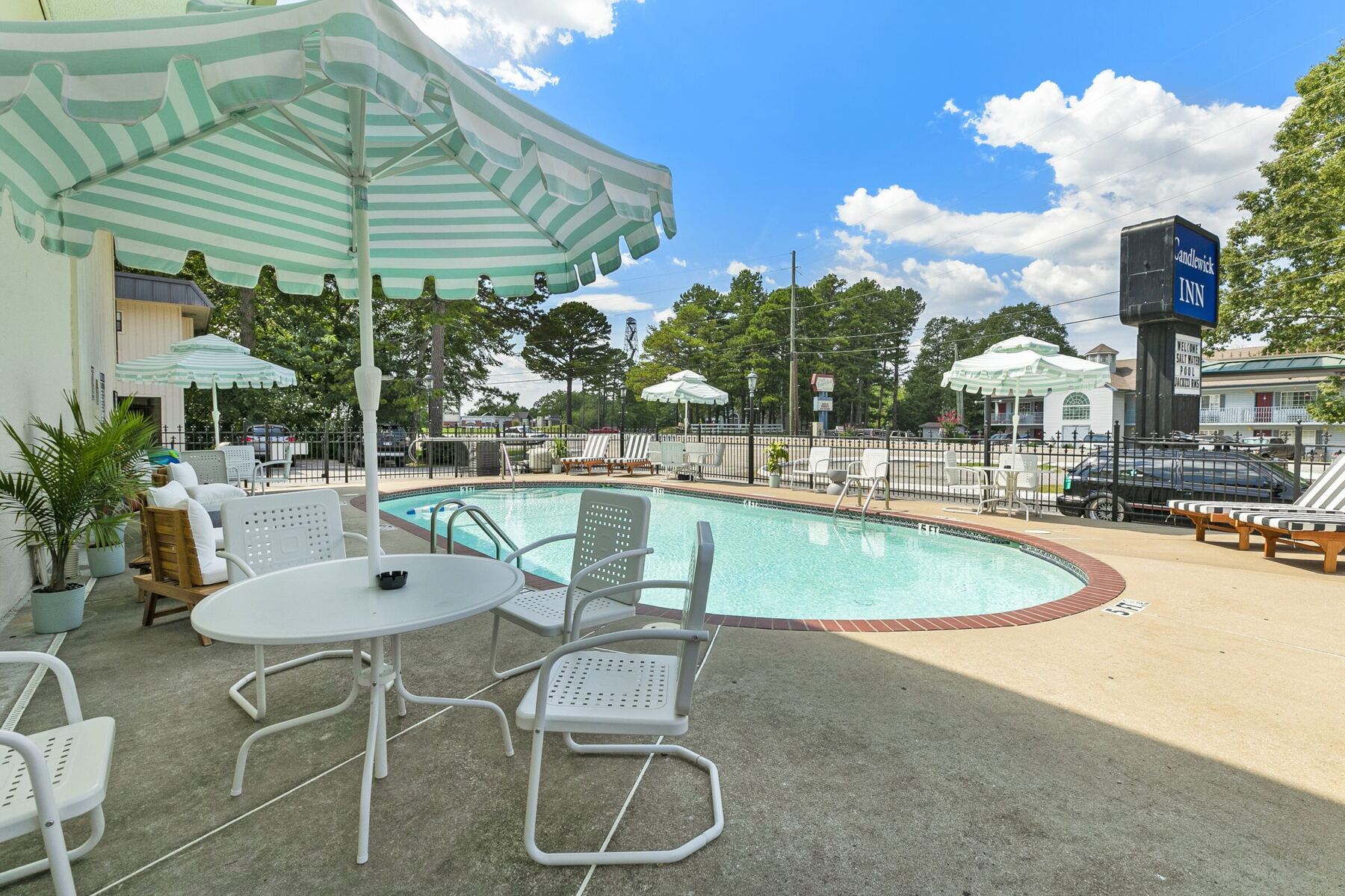 The Candlewick Inn pool with striped umbrellas and white patio chairs on a sunny day